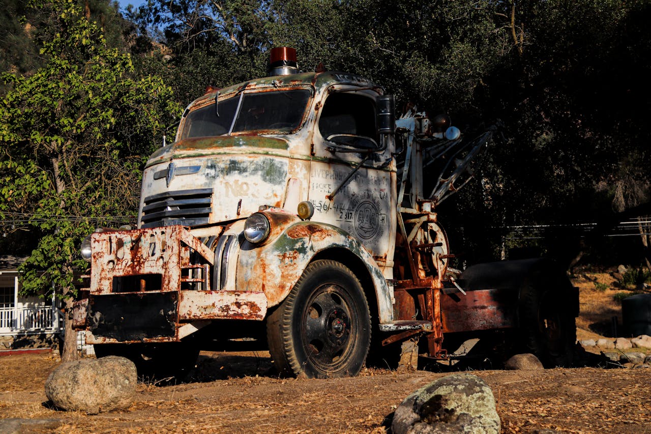 A rusty, abandoned tow truck sits outdoors, surrounded by nature and vintage charm.